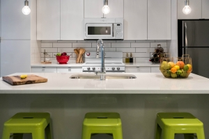 A kitchen with three stools at the island with pendant lighting and subway tile back splash